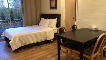 Un dormitorio con cama, una mesa y sillas. Se ve una ventana con cortinas, una puerta y un cuadro en la pared.