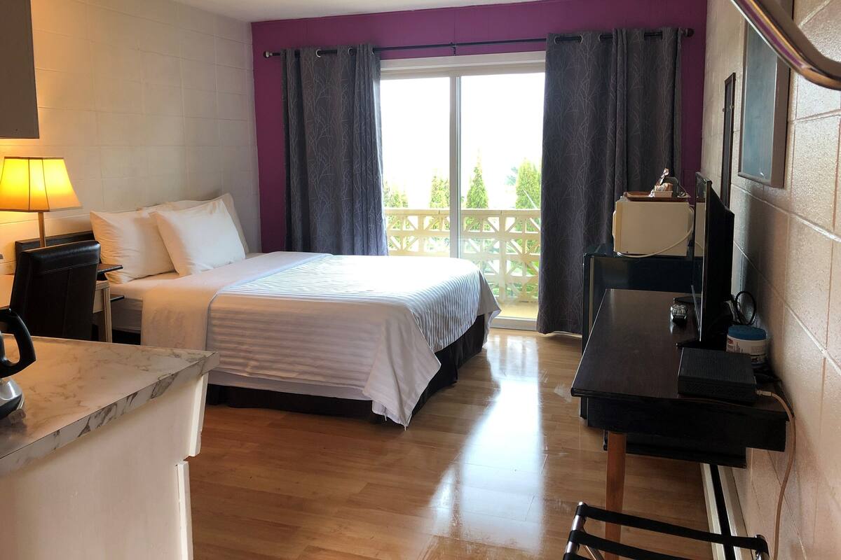 A hotel room with a bed, a desk with a computer, a lamp, and a view of the outside.