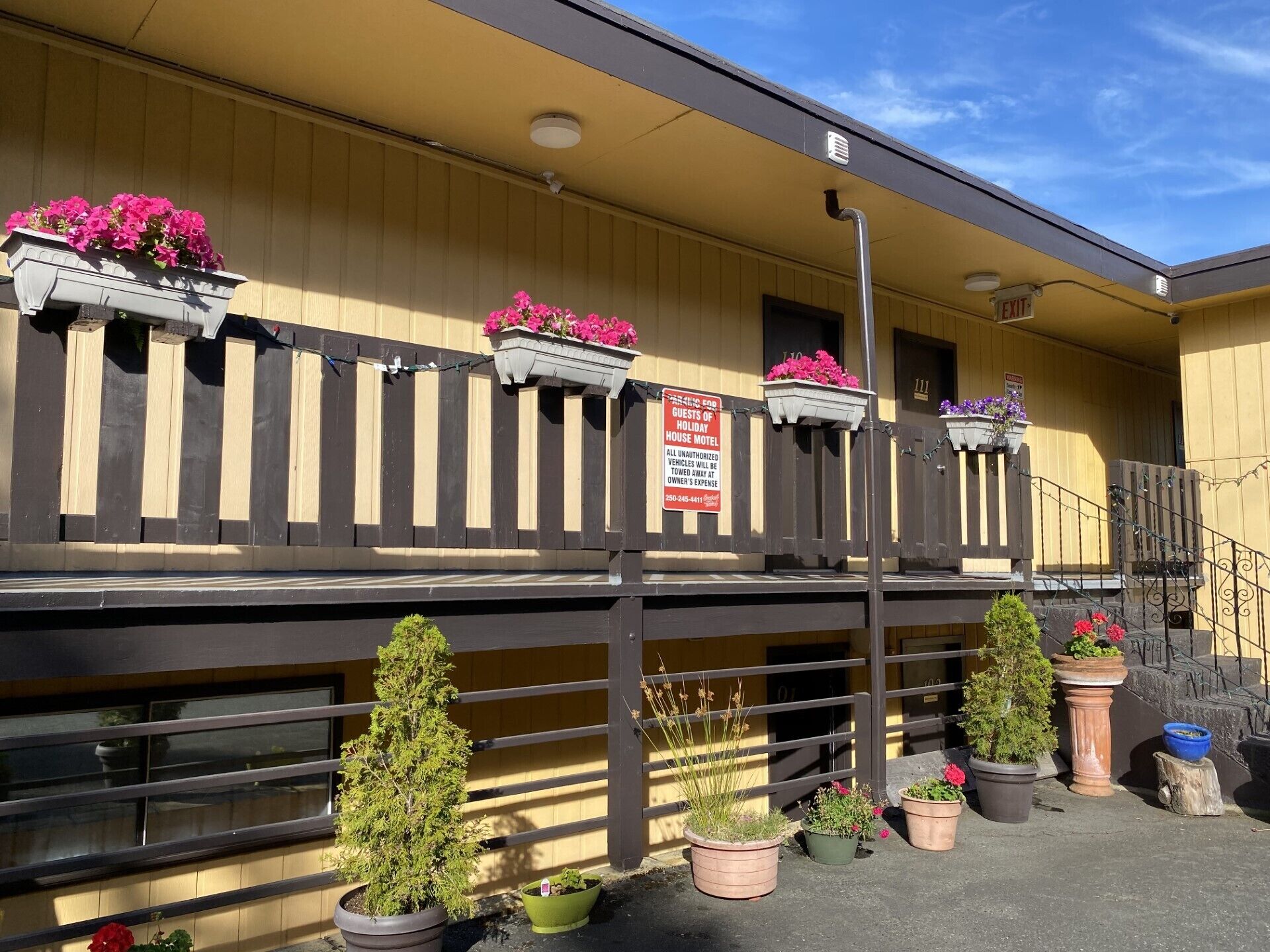 A motel with a balcony, potted plants, and a sign indicating guests of the motel.
