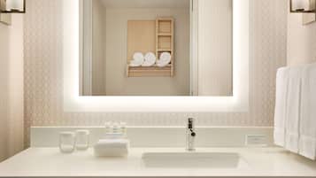 A modern bathroom with a large mirror, a white sink, and a wooden shelf with towels.
