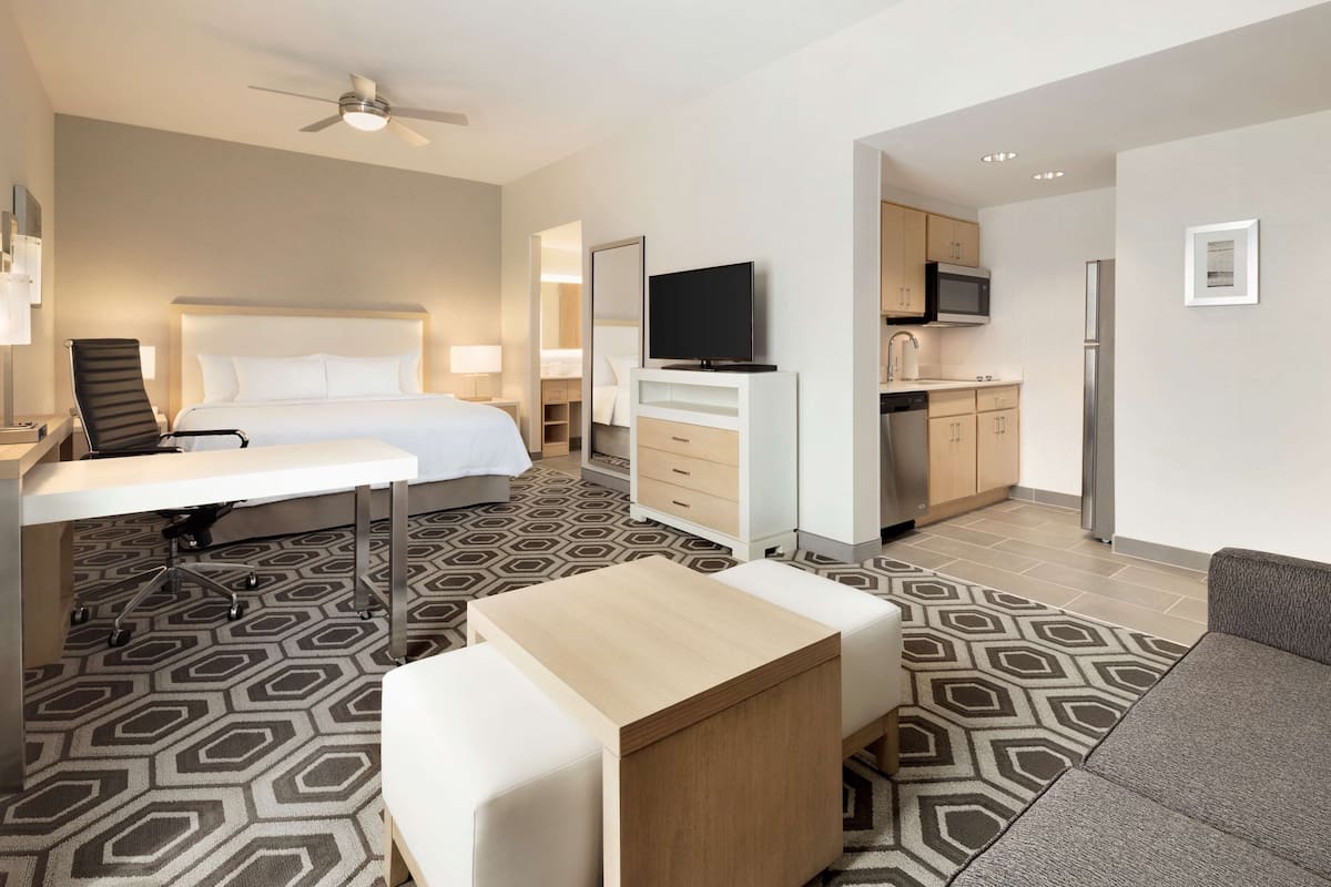 A hotel room with a bed, desk, chair, TV, kitchenette, and a sofa.