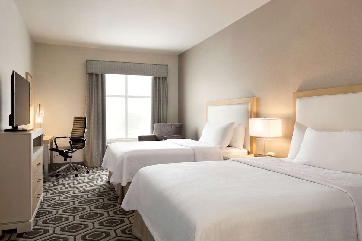 A hotel room with two beds, a desk, a chair, a television, and a window with curtains.