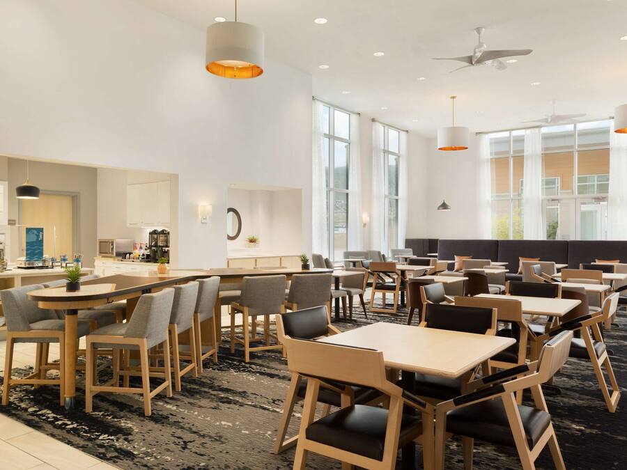 Un espace de restauration moderne, doté de plusieurs tables et chaises, de grandes fenêtres et de ventilateurs de plafond.