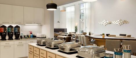 A modern kitchen with white cabinets, stainless steel appliances, and a breakfast bar. There are various kitchen utensils and appliances visible.