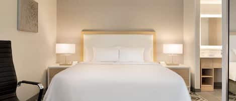 A hotel room with a large bed, two bedside lamps, a chair, and a bedside table.