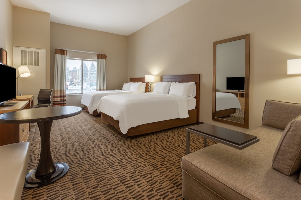 A hotel room with two beds, a desk, a chair, a sofa, and a large mirror.
