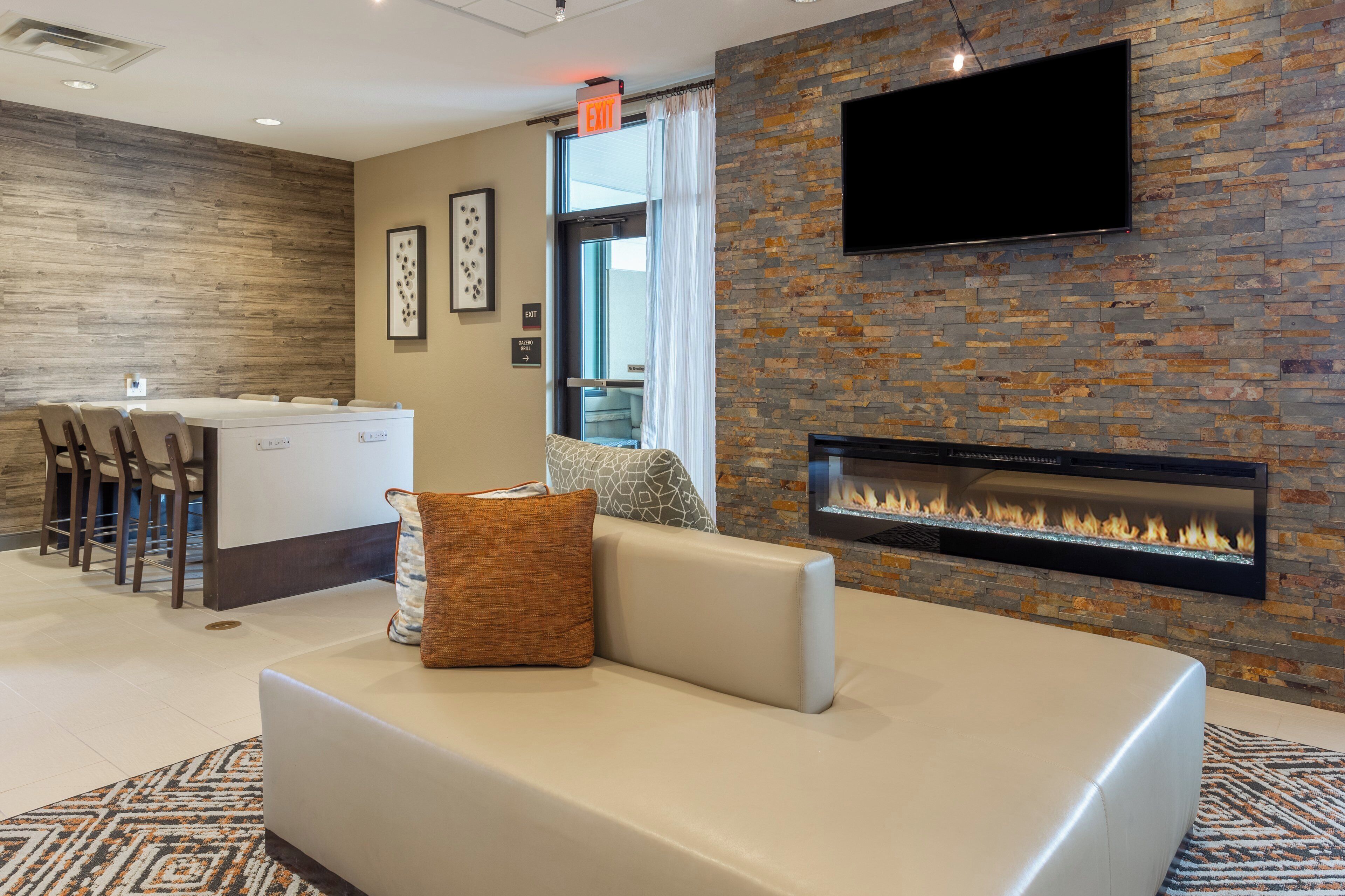 Una sala de estar moderna con chimenea, un televisor de pantalla plana montado en la pared y un comedor con mostrador de cocina y sillas.