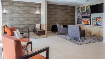 A modern lobby with seating arrangements, a wall-mounted TV, and artwork.