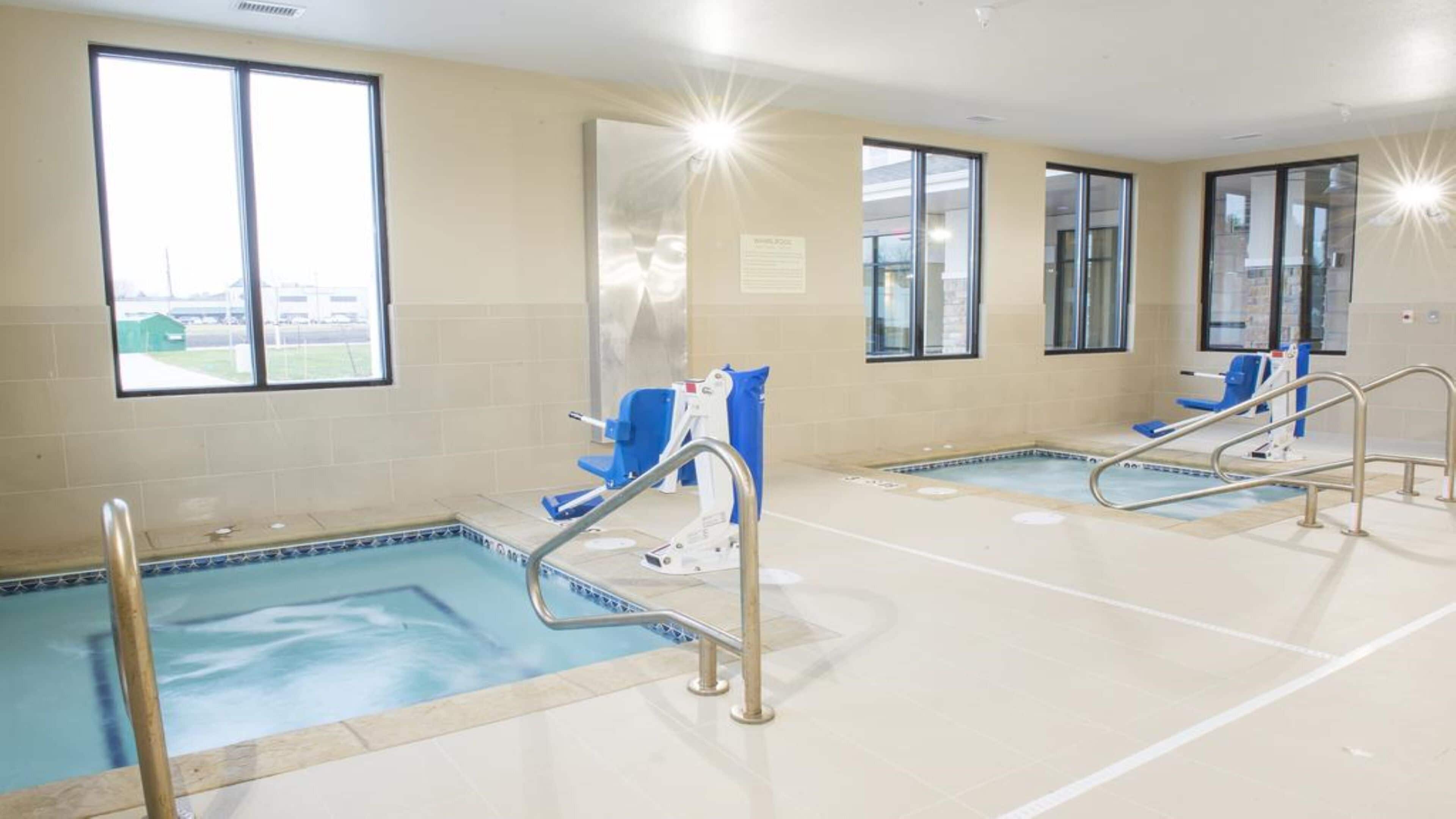 A swimming pool area with two pools, each with a blue chair and a metal ladder.