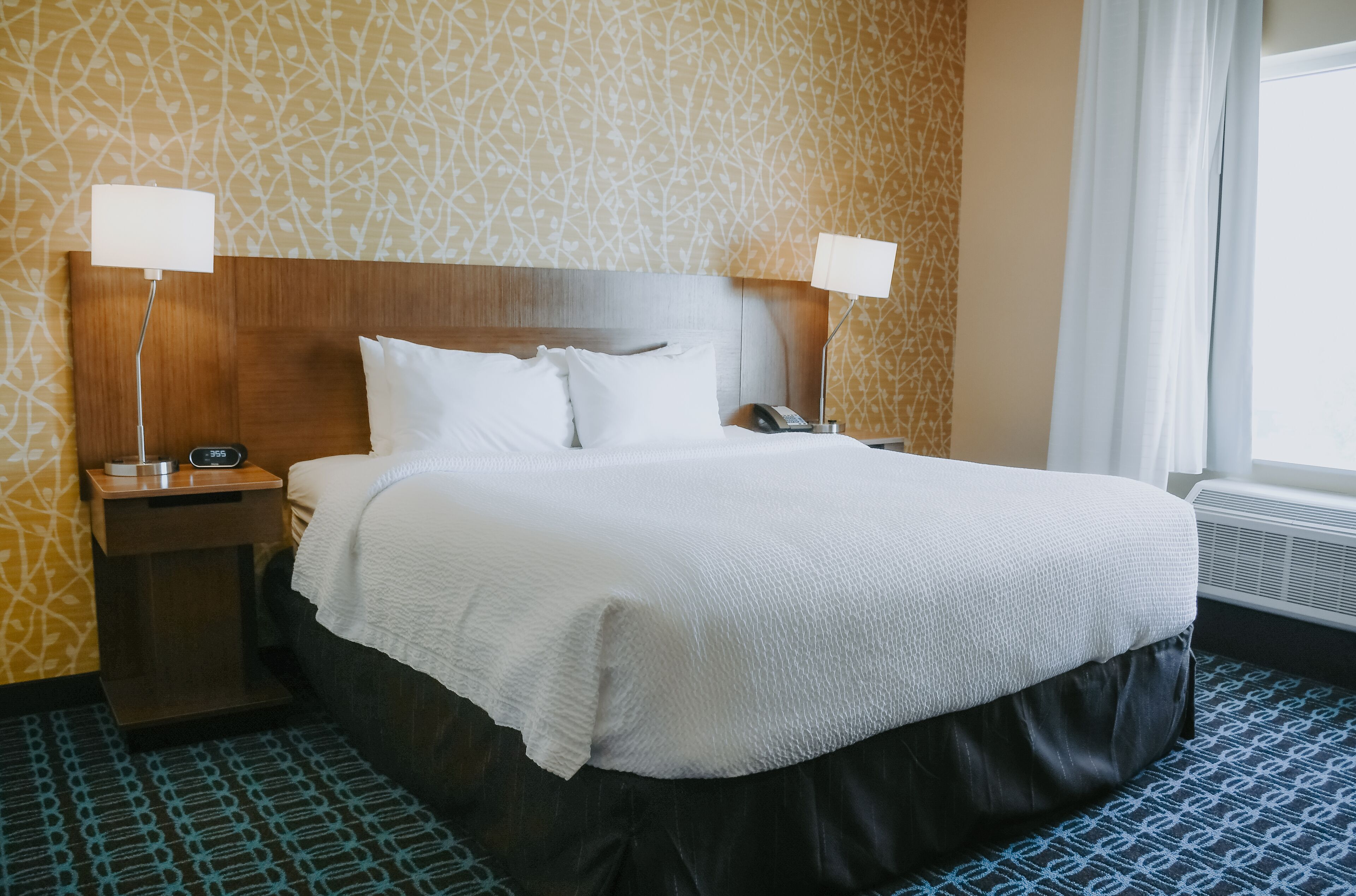 Une chambre d’hôtel avec un grand lit, deux tables de chevet avec des lampes, un téléphone et une fenêtre avec des rideaux.