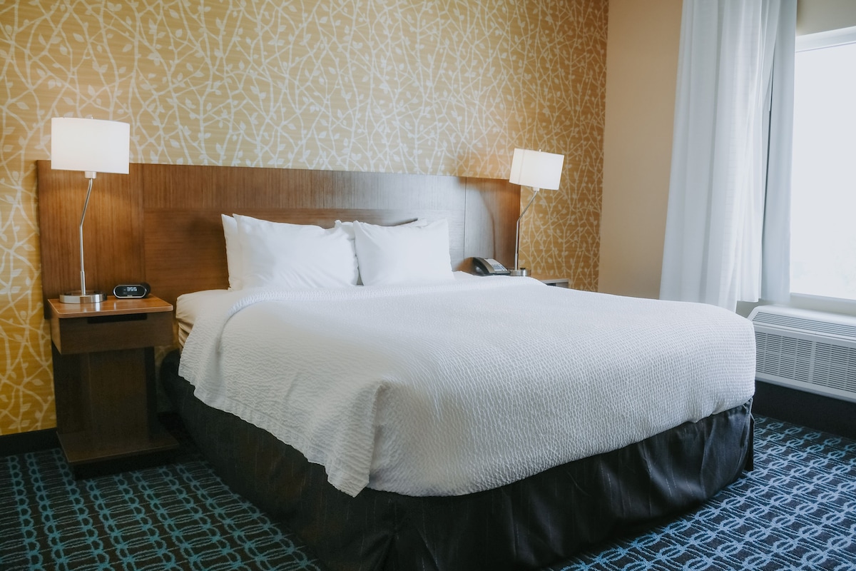 A hotel room with a large bed, two bedside tables with lamps, a telephone, and a window with curtains.