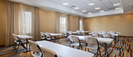 A conference room with tables and chairs, large windows with curtains, and a patterned carpet.