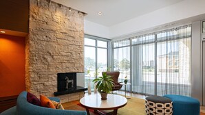 Una sala de estar moderna con una pared de acento de piedra, una chimenea, una mesa redonda y un ventanal con cortinas.