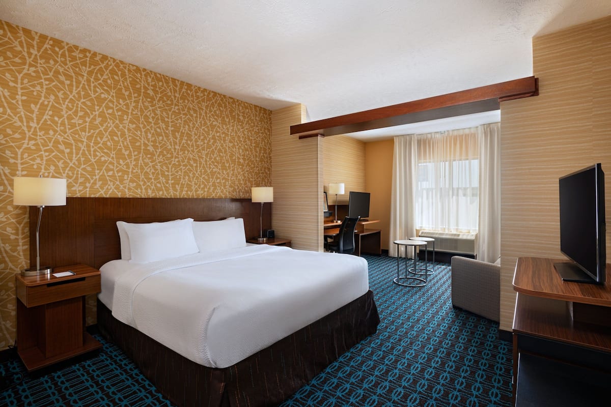 Habitación de hotel con una cama grande, un escritorio con silla, televisión y ventana con cortinas.
