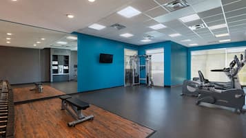 Een sportschool met trainingsapparatuur, een spiegel en een televisie aan de muur.