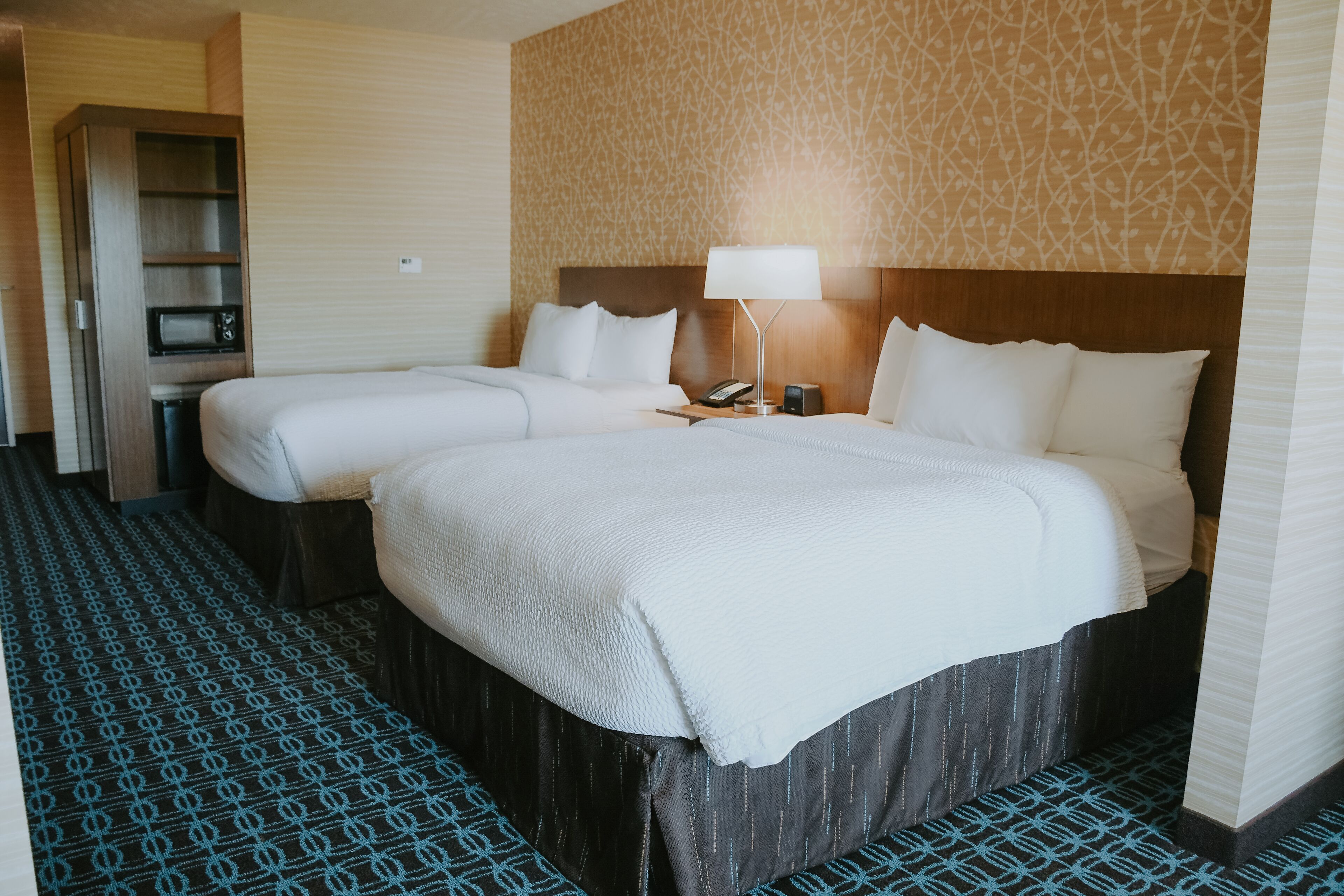 Una habitación de hotel con dos camas, un escritorio, una lámpara y un minibar.
