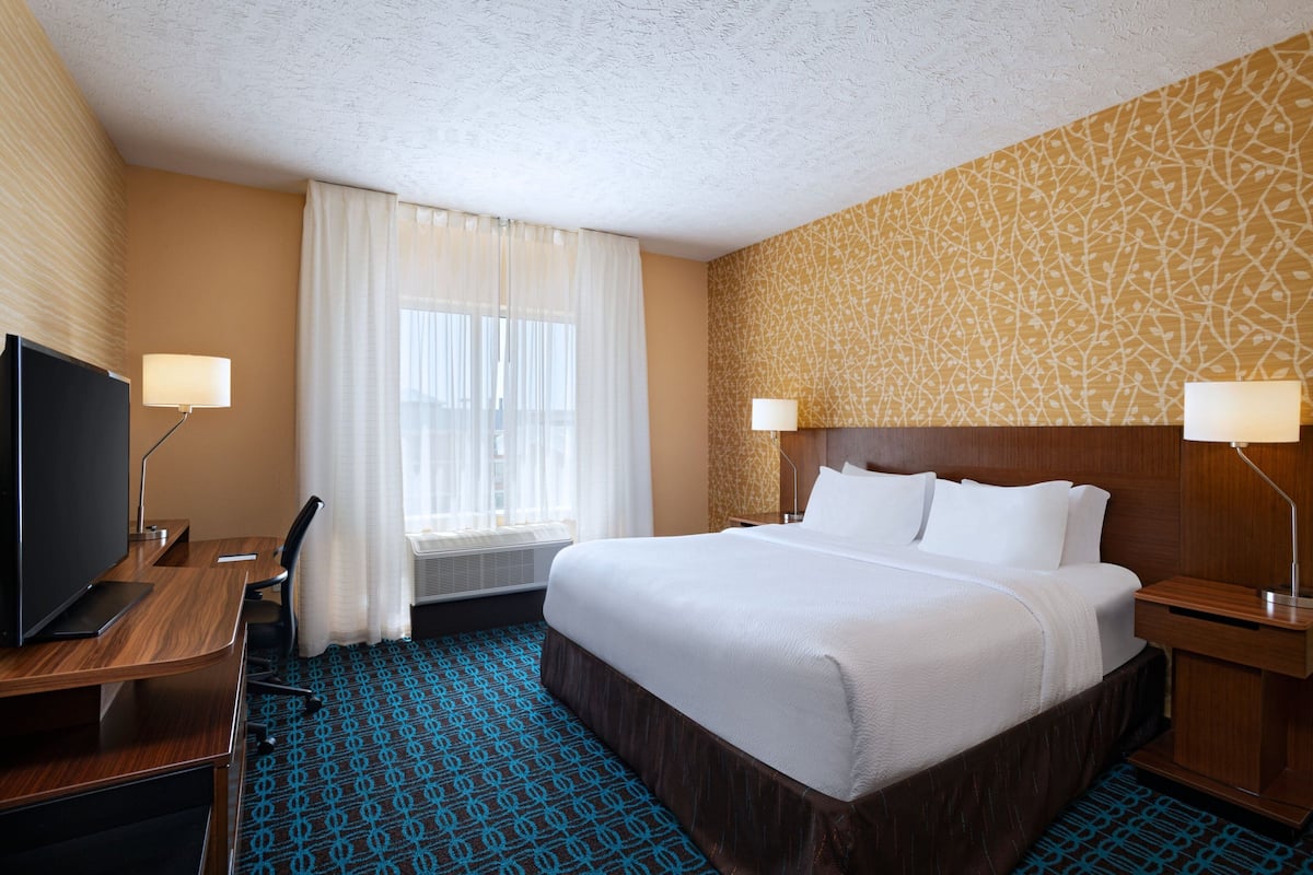 Una habitación de hotel con una cama grande, un escritorio con televisor y una ventana con cortinas.