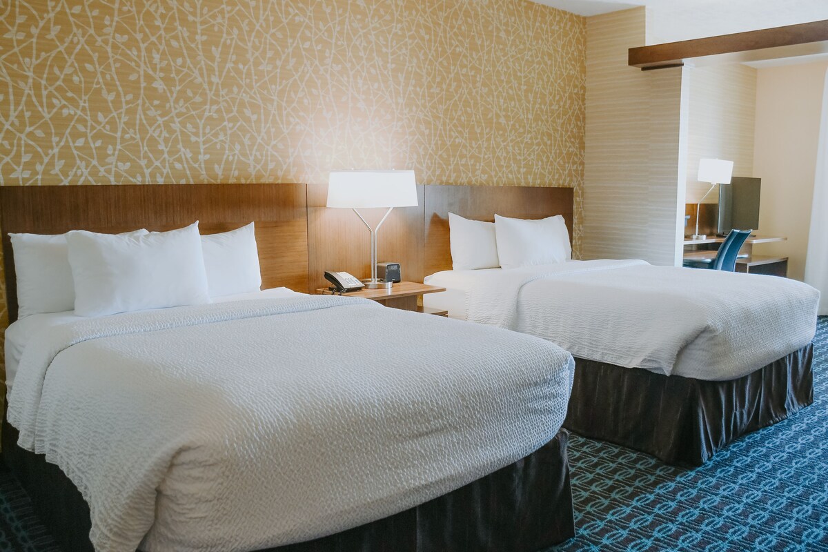 A hotel room with two beds, a desk, a chair, and a telephone.