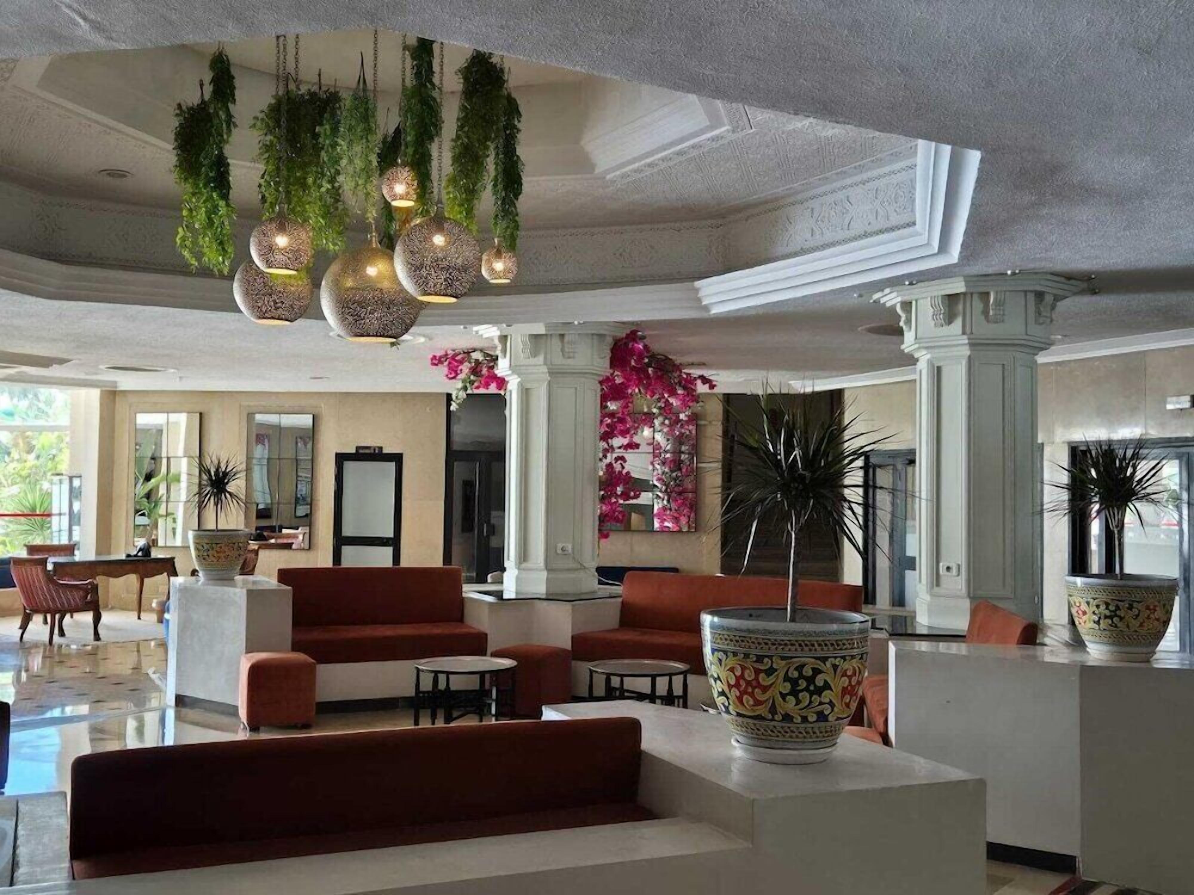 Un hall d’entrée spacieux, doté de sièges rouges, de plantes suspendues et d’un grand vase décoratif.