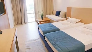 Et hotelværelse med to senge, et skrivebord, en stol og et vindue med gardiner.