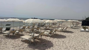 En strand med rækker af liggestole og parasoller, sand og havet i baggrunden.