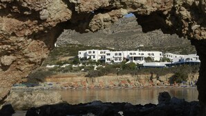 A coastal hotel with white buildings, a beach with umbrellas, and rocky cliffs. - Argo (Karpathos)