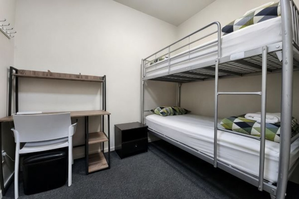 A bunk bed with a desk and chair, a small table, and a shelf.