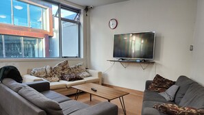 A modern living room with a sofa, a coffee table, and a TV mounted on the wall. - Newton Lodge Auckland - Hostel (Auckland)