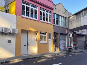 Un bâtiment portant l’inscription « PILOT PRESS », un commerce fermé avec une pancarte indiquant « 27 », et une rue avec un trottoir et un bordure.