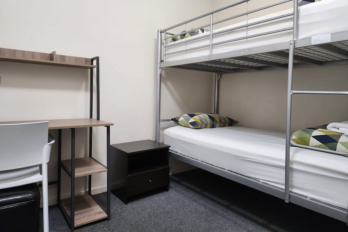 A bunk bed room with a desk and chair, a small black cabinet, and a wooden shelf.