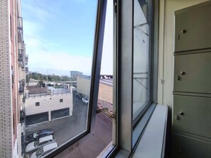 A view from a window overlooking a parking area with several cars, a building with a flat roof, and a clear sky.
