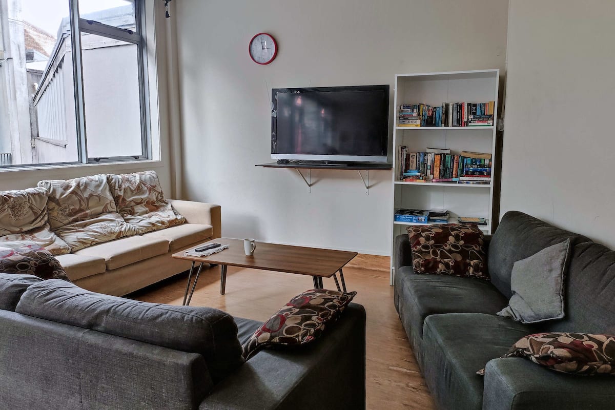 A living room with a sofa, a coffee table, a bookshelf, and a TV mounted on the wall.