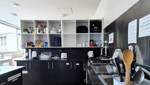A modern kitchen with black cabinets, a stainless steel sink, and a variety of kitchen utensils and appliances. - Newton Lodge Auckland - Hostel (Auckland)