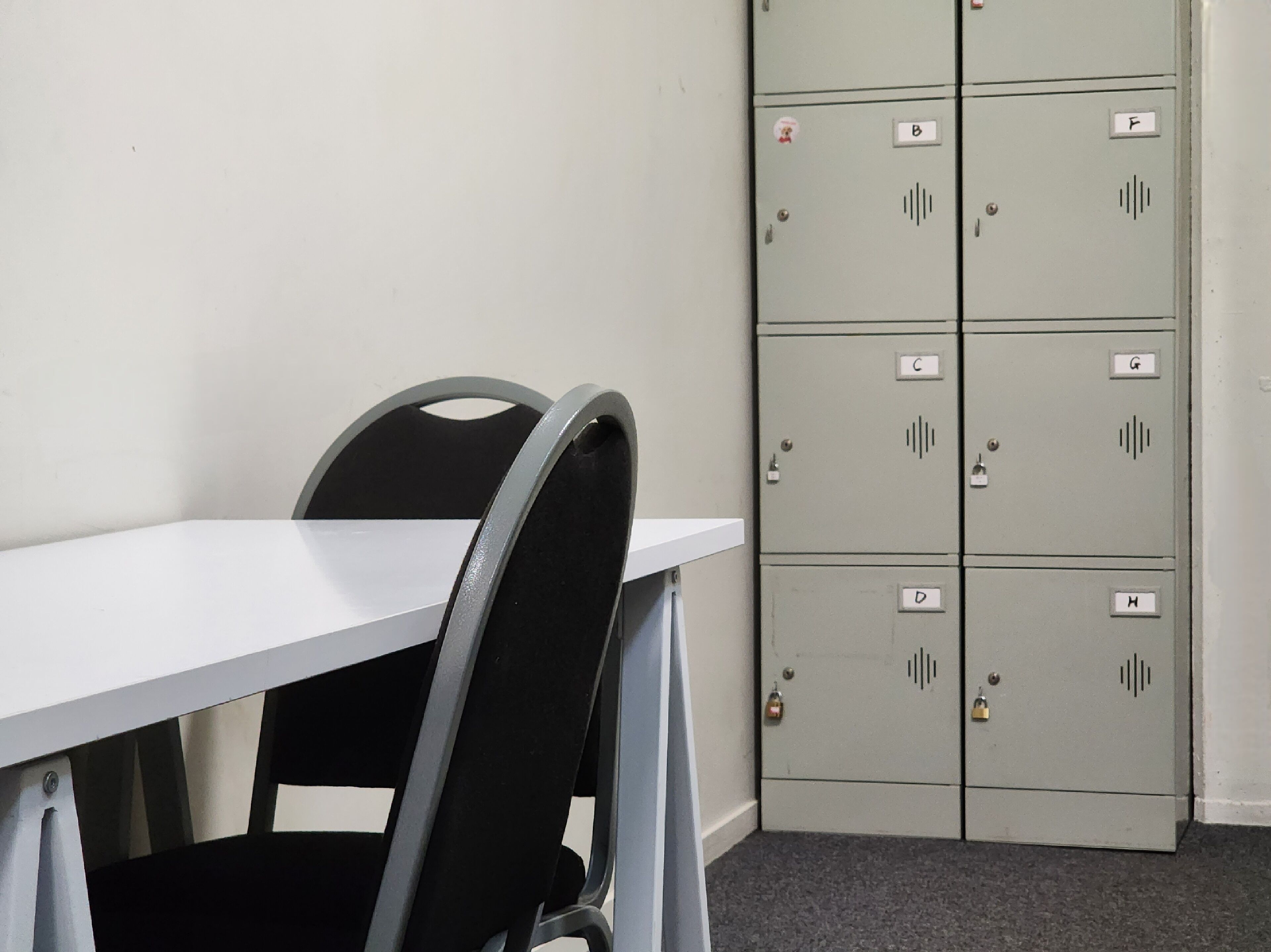 A room with a white table and a black chair, and a set of grey lockers with labels.