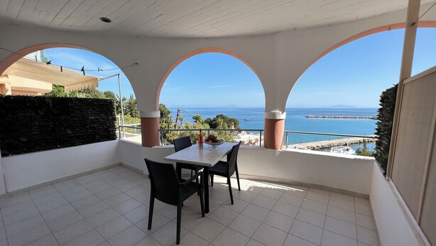 A balcony with a table and chairs, a stone wall, and a view of the sea. - Harbour View (Kefalonia)