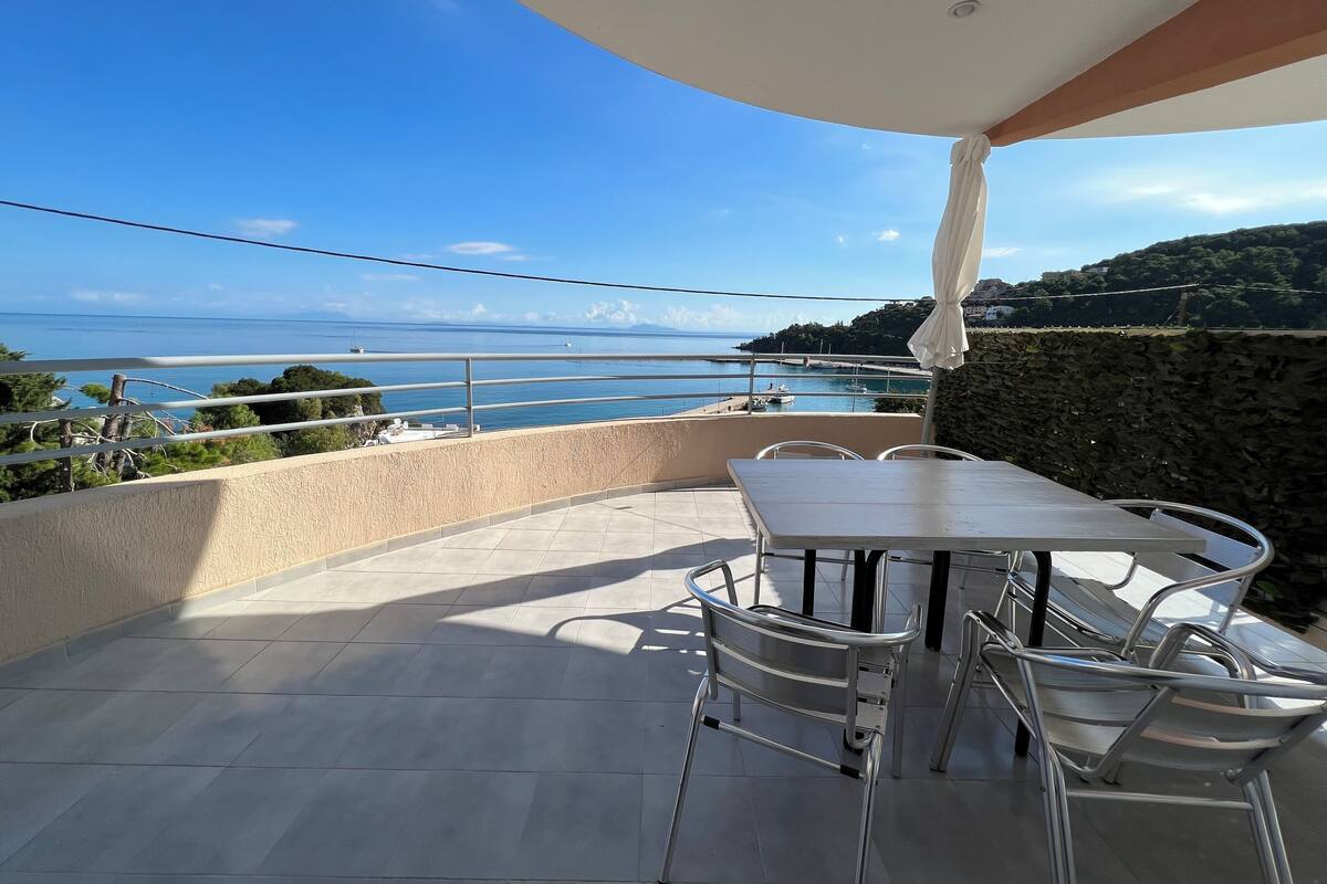 Um terraço com mesa e cadeiras, vista para o mar e uma parede de pedra.