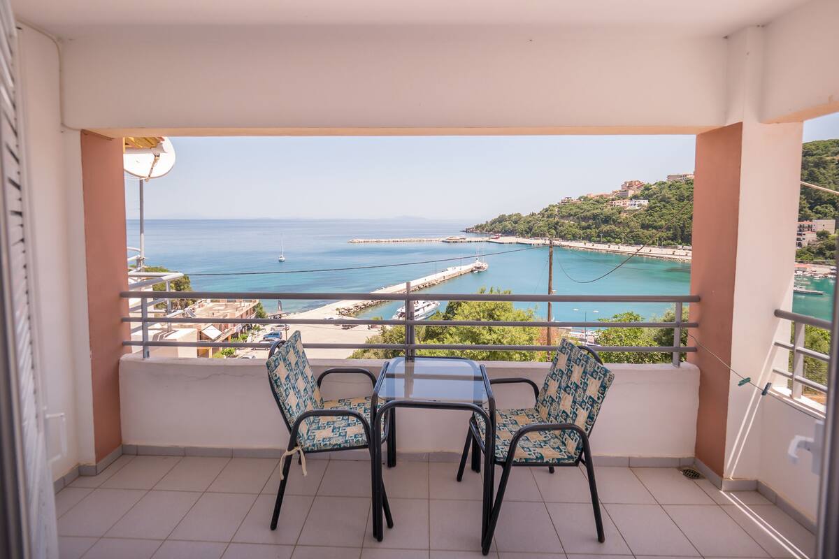 Varanda com duas cadeiras e uma mesa, com vista para a costa, uma praia e um cais.