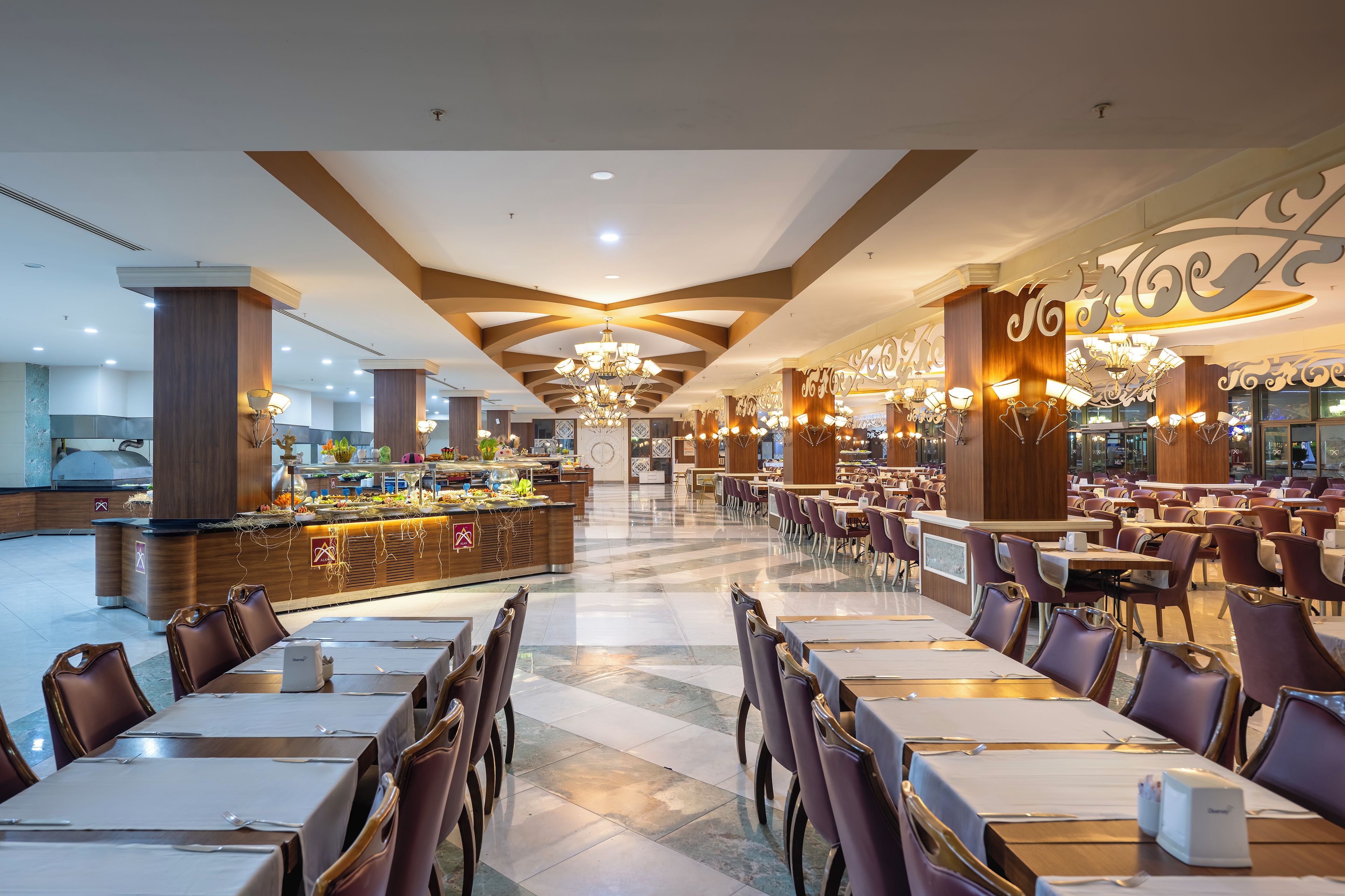 Ein geräumiger Hotel-Speisesaal mit mehreren Tischen und Stühlen, einer zentralen Bar und dekorativen Deckenverzierungen.