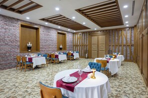 A dining area with round tables, chairs, and a brick wall. - Alan Xafira Deluxe Resort & Spa (Alanya)