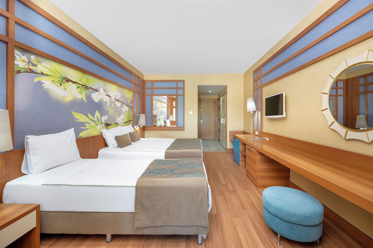 Une chambre d’hôtel avec deux lits, une télévision, un miroir et un tableau représentant des fleurs accroché au mur.
