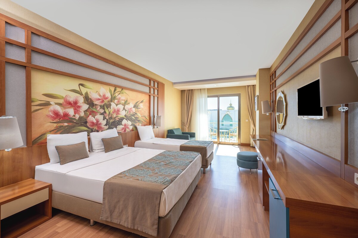 Une chambre d’hôtel avec deux lits, une télévision, un bureau et une grande fenêtre.