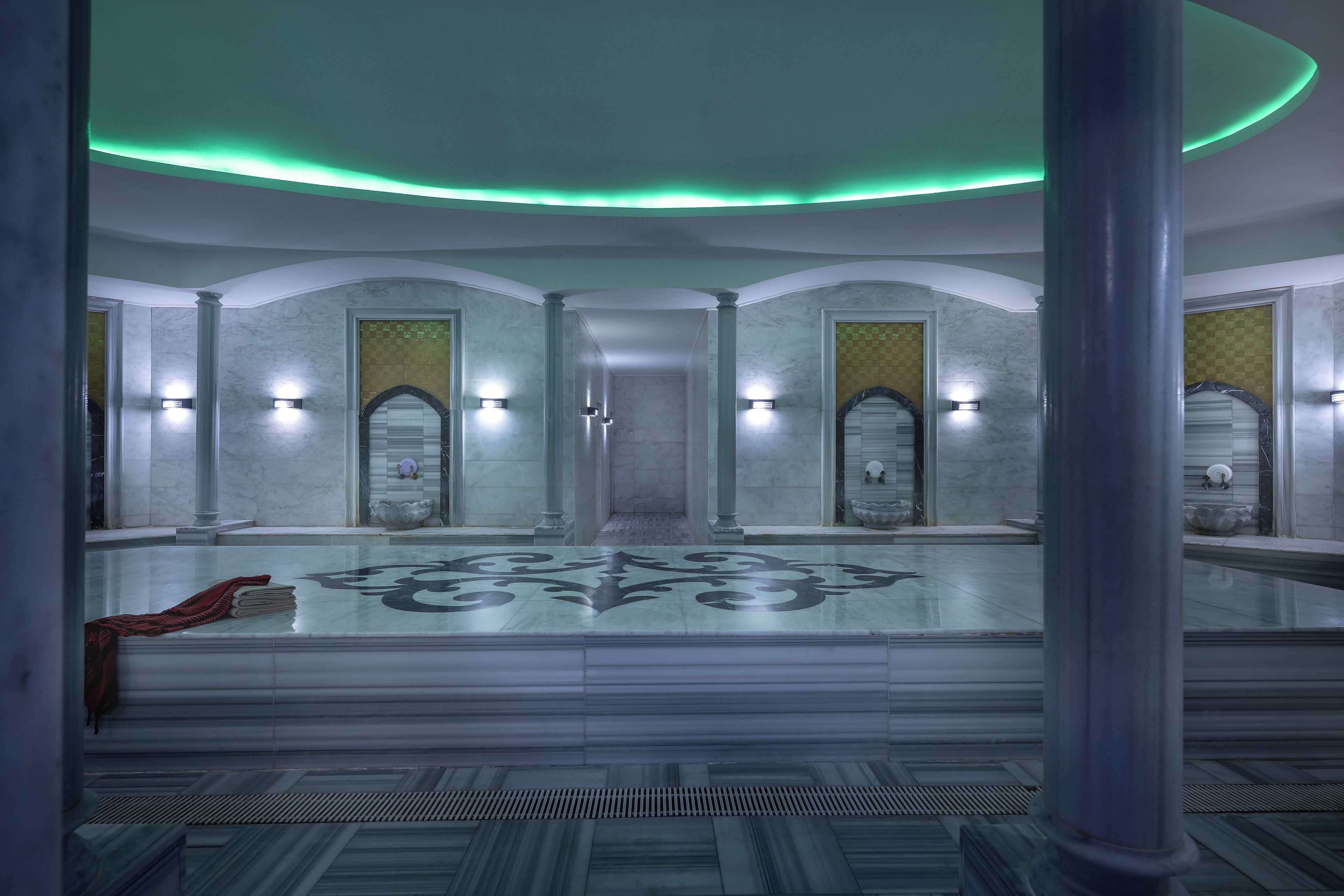 Eine großzügige Lobby mit Marmorboden, einer zentralen Säule und einer grün beleuchteten Decke.