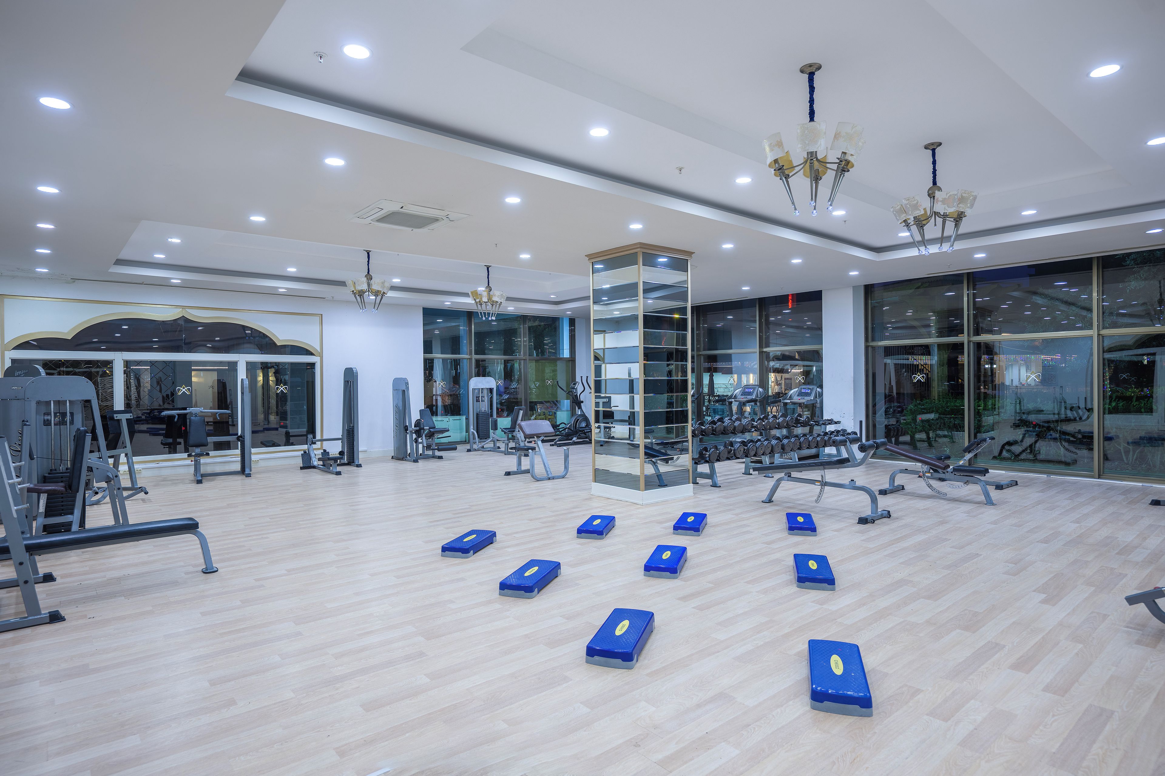 Ein Fitnessraum mit Trainingsgeräten, Holzboden und großen Fenstern.