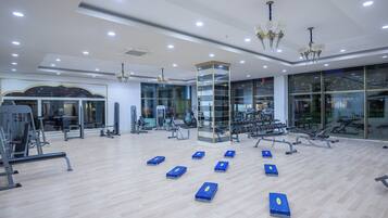 Ein Fitnessraum mit Trainingsgeräten, Holzboden und großen Fenstern.
