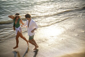 Una pareja caminando por una playa, con olas al fondo.