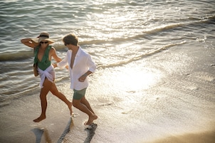 Um casal caminhando na praia com ondas ao fundo.