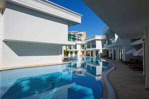Un hotel moderno con piscina, mobiliario exterior y un cielo azul despejado.