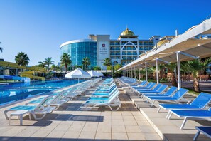 A swimming pool with lounge chairs and umbrellas, a hotel building with a dome, and palm trees.