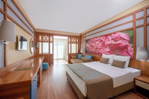 A hotel room with a large bed, a desk, a chair, and a view of a garden through a sliding door. - Alan Xafira Deluxe Resort & Spa (Alanya)