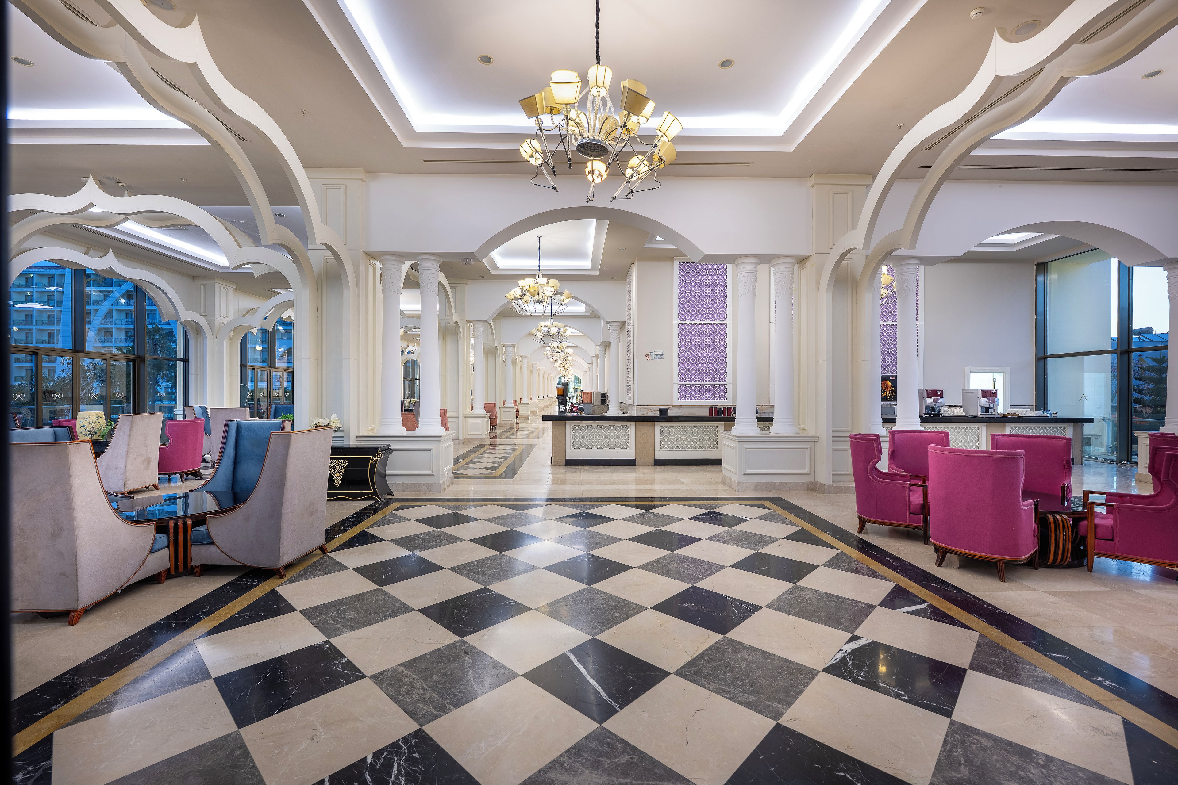 Eine großzügige Lobby mit Schachbrettmuster-Boden, einer Rezeption und Sitzbereichen mit modernen Stühlen.